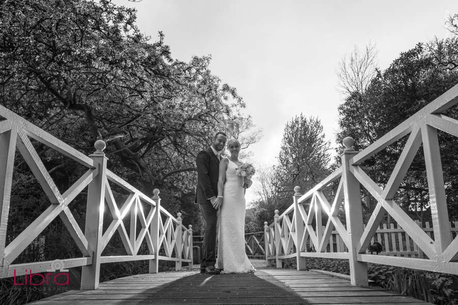 Bride and groom pose on bridge in b&w
